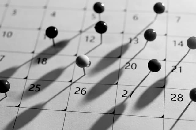 Close up of a calendar with several dates marked by pushpins.