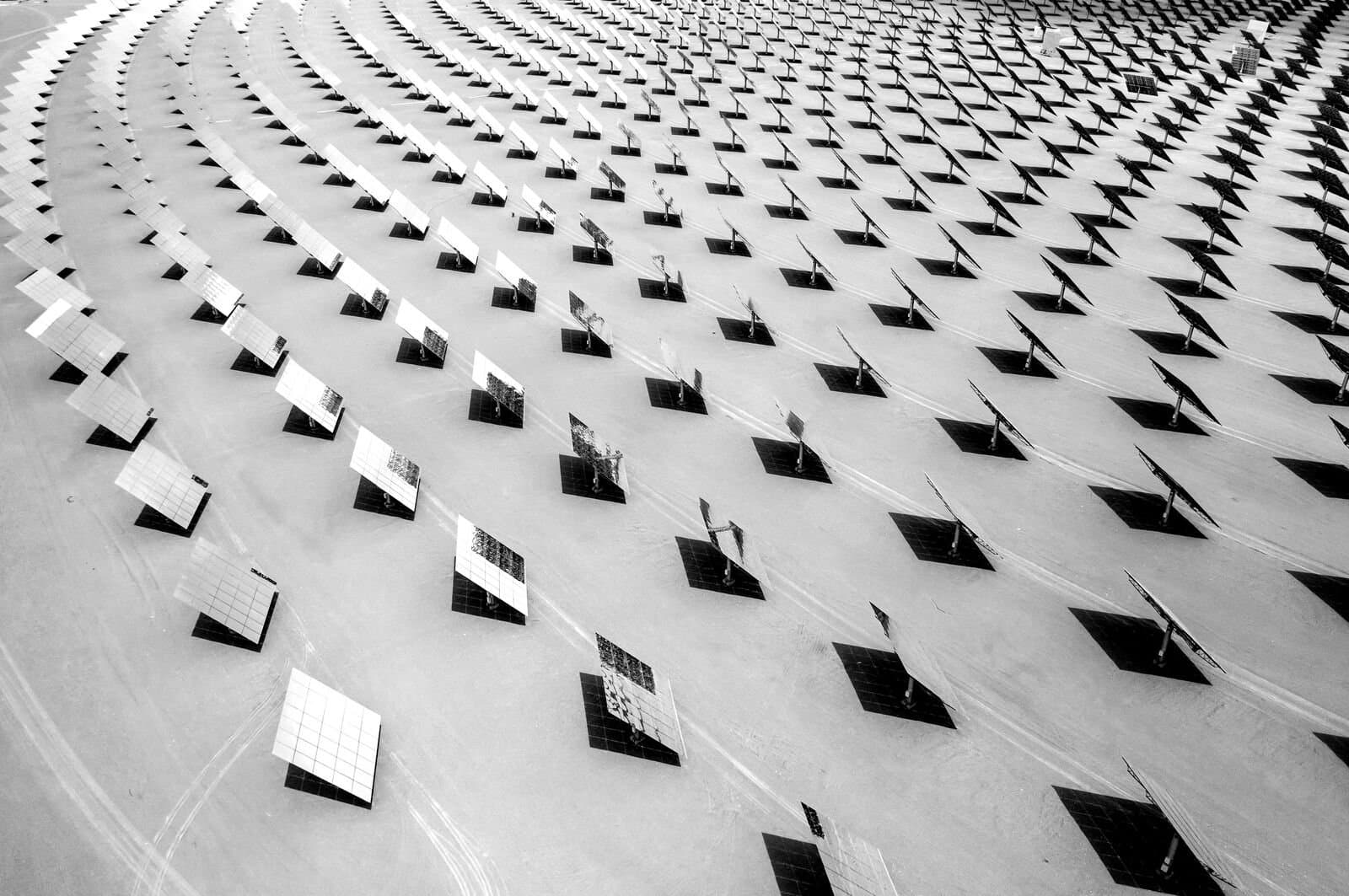 Hundreds of solar panels, with their shadows being cast behind them