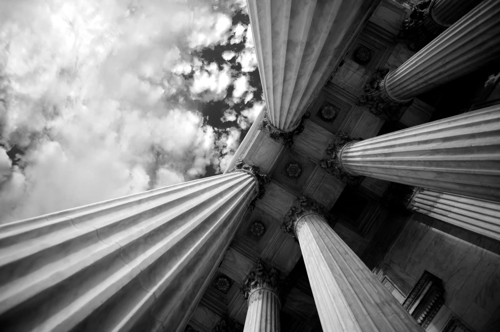 low-angle view of large classical stone columns supporting a historic building beneath a cloudy sky.