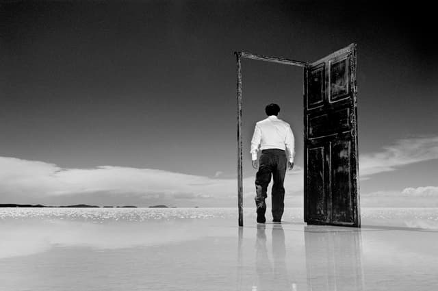 Man walking through a door standing alone in a vast reflective landscape, suggesting transition or new beginnings.