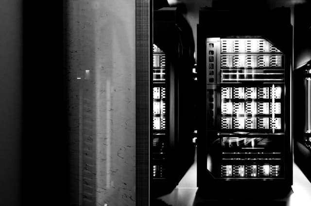 Dimly lit server racks glowing with internal lights, viewed through a partially open sliding door.